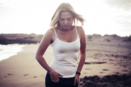 blonde long hair beautiful girl look at you walking near the coastline on the beach. Golden hours with ocean, waves and summer style conceptの写真素材