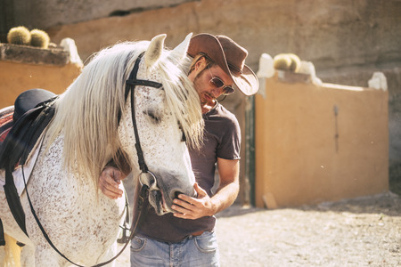 beautiful man like cowboy speak with his best friend horse before ride it over the mountains. sunny day and backlight. live in the nature and with animals concept. alternative lifestyleの写真素材