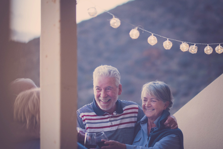 outdoor terrace with golden light and four adult seniors men and woman staying together with joy and happiness drinking wine togetherの写真素材