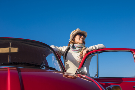 40s woman hippy style enjoy the weather outside of her old red car. Vintage life and style, blue clear sky backgroundの写真素材