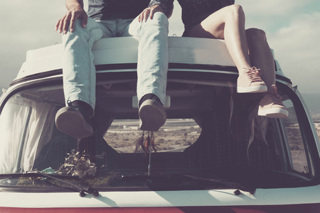 enjoy the vanlife. two pair of young legs sitted on the top of a vintage retro van enjoying the day. travel and discover new places like a desert in background. every morning new world wake up.の写真素材