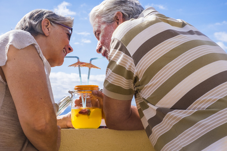 man and woman aged 60 years old woman drinking healthy fruit from a glass vase outdoor in the terrace. nice view and beautiful people.の写真素材