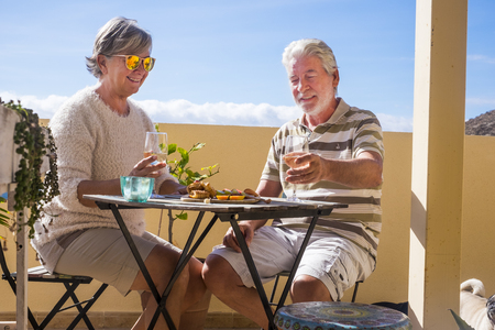 senior 70 years old wine drink glass goblets sitting at the table in a sunny terrace with green plants. relaxed life concept and food on the tableの写真素材