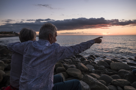 two senior people sitting on the beach at sunsetの写真素材