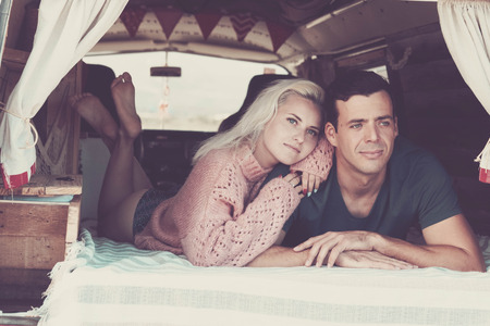 beautiful caucasian couple lay down lookig the landscape natural scene from a vintage van in vanlife lifestyle. freedom and alternative life or vacation concept in conctact with the worldの写真素材
