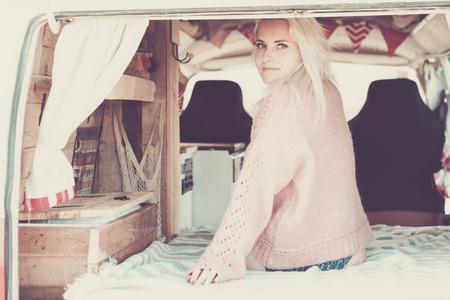 lonely beautiful blonde model girl with blue eyes sit down inside an old vintage camper to travel and discover the world. wanderlust concept and vanilife choice for young people all over the worldの写真素材