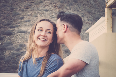 love whisper and secret concept for a young man and woman outdoor on the terrace. vintage filter for romantic scene. blonde beautiful demale smiling.の写真素材