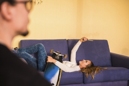 blonde young beautiful lady lay down on the sofa outdoor using a mobile phone to take selfie. skateboard and youth conneteced concept. vacation and leisure. focus on the girl.の写真素材