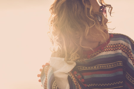 hippy mexican style poncho wearing for beautiful model middle age nice woman outdoor with wind in the air and unglasses during a golde sunset. vintage style filter and backlight portrait pictの写真素材