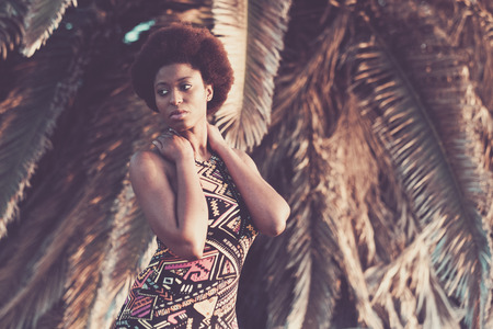 beautiful african black skin race model pose in fashion style with coloured dress with a tropical palm natural background. outdoor summer beauty in vacation conceptの写真素材
