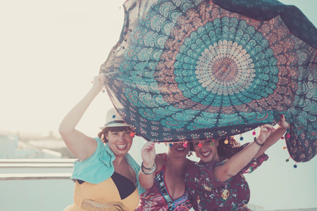 three young beautiful female ladies take a mandala textile over the heads. playing with the wind in outdoor activity. summer concept with sun backlightの写真素材