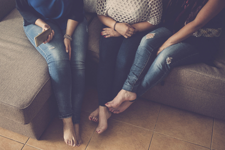 friendship concept for three caucasian women at home sitting on the sofa and speaking about stories. lifestyle and together leisure time concept. nude feet and mobile phoneの写真素材
