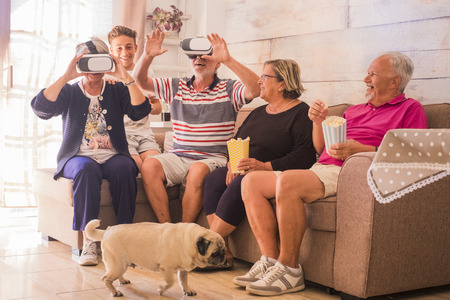 group of people mixed generation from senior to teenager having fun at home trying modern technology goggled headset on the sofa. laugh and smile and a pug walking on the groundの写真素材