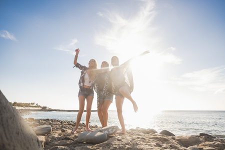 Group of three beautiful nice young woman jumping for fun and happiness, independent life together in friendship. Tenerife stone beach in a sunny day, enjoy the time.の写真素材