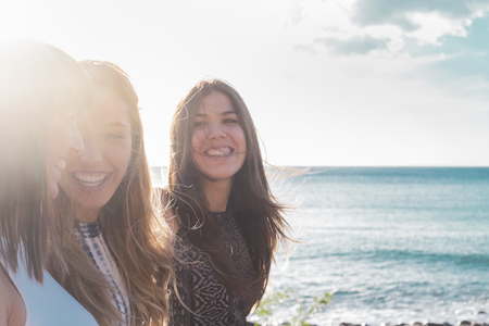 3 young women walk on the beach looking at each other, laughing and spending free time together. on a nice summer day. with sun and sea as a background.の写真素材