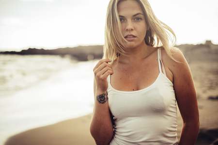 blonde long hair beautiful girl look at you walking near the coastline on the beach. Golden hours with ocean, waves and summer style conceptの写真素材
