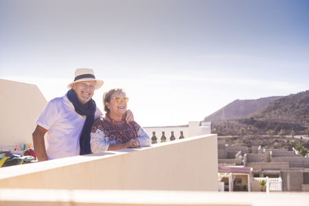 senior couple having some time on the rooftop at home with view on other buildings in contruction and mountains. sunlight and plants and nature outdoor.の写真素材