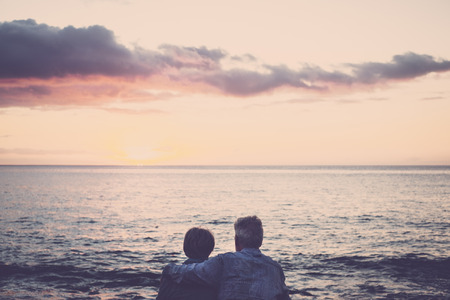 elderly couple sitting in front of the sea at sunsetの写真素材