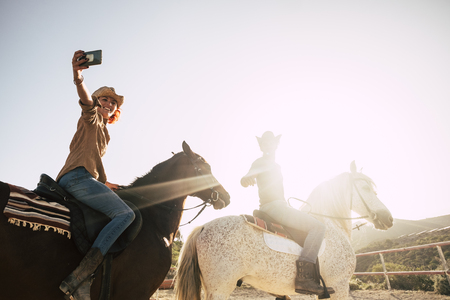 beautiful caucasian coule riding horses equestrian outdoor during a sunny day and sunset time. leisure activity taking selfie picture in happiness and nice lifestyle enjoying the nature and the animalsの写真素材