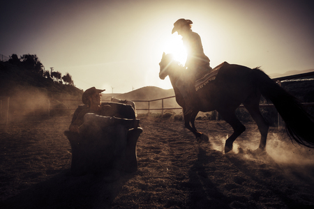 hero concept dramatic and advertising style image for cowgirl making dust riding a horse near a cowboy sit down on a chair in the middle of the track. another horse in background. alternative leisure activityの写真素材