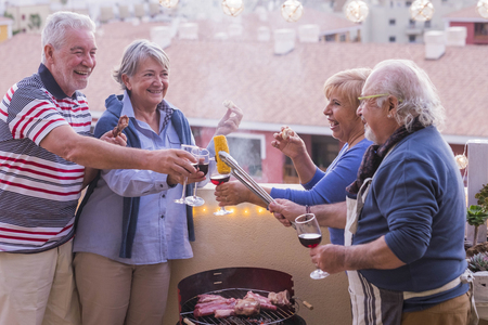 four active senior retired have fun in the terrace at home cooking some bbq everybody smiles and stay together in friendship under a nice sunny day.  vacation and relationship people conceptの写真素材