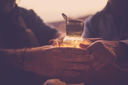 8 joined hands hold a small glass jar containing a yellow light.の写真素材
