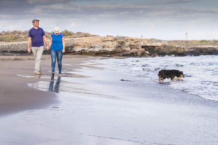 nice couple caucasian walking down the beach on the shore barefoot naked foot with best friends border ollie dog play with the waves in a summe vacation time in tenerifeの写真素材