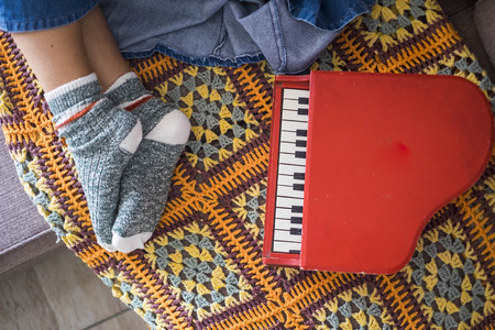 woman relaxed feet with nice socks at home in rest position. little piano toy on the sofa near her. music and artist life with pattern cover with vintage colors and background. lifestyle happy at homeの写真素材