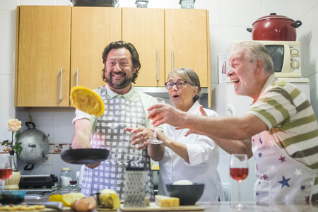 carzy moment funny group of middle age man and two senior man and woman. omelette flying during the cook f the dinner. kitchen play togetherの写真素材