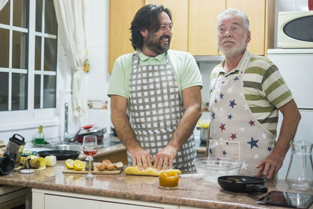 Two man at work in the kitchen adult and senior. Son and father cook together with smilies and surprise at home. daily family life conceptの写真素材