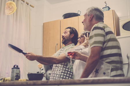 Flying eggs in the kitchen for a crazy and funny dinner prepared by three senior at home. Warm tones for family scene. Home food cook.の写真素材