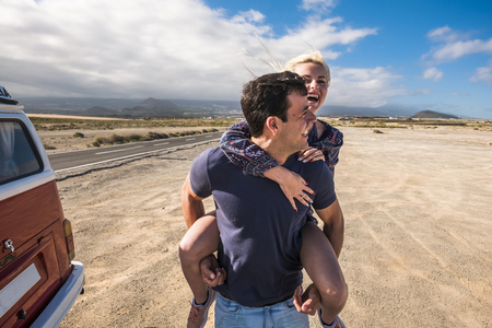 nice caucasian beautiful model couple in love play and stay together in leisure activity outdoor near a long road crossing the desert in a long trip vacataion with old alternative camper van. freedom and indeendence for young peopleの写真素材