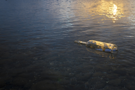 transparent glass bottle with a message closed by rope carried by the sea and found ashore on a pebble beachの写真素材