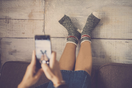young nice caucasian lady on the sofa taking picture with smartphone at her feet with happy and funny socks. home daily scene in fun lifestyle. share life with friends conceptの写真素材
