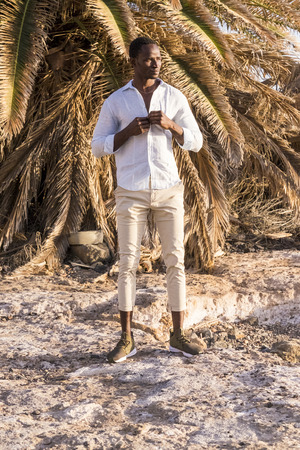 beautiful high black race model pose on a tropical place with palm background. warm yellow colors in a sunny day. fashio concept for nice style of dressの写真素材