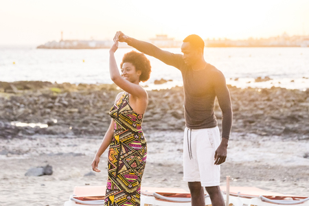 happy nice beautiful black african race couple enjoy and dance at the sea during a golden coloured outdoor sunset. happiness and friendship relationship concept. vacation leisure timeの写真素材