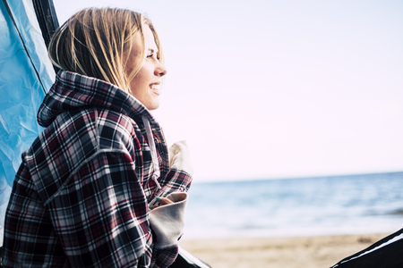 beautiful young blonde woman outside hug herself enjoying freedom and vacation leisure time in the summer. camping free for alternative vacation on the beach near the waves of the oceanの写真素材
