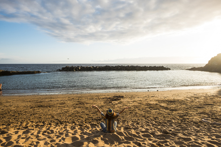 lonely wanderlust woman in total happiness and freedom sitting on the beach with sunset and ocean in front of her. nice lifestyle for beautiful lady enjoying the nature and the world. travel concept.の写真素材