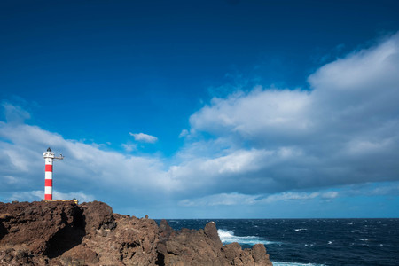old style classic lighhouse on the coast of Tenerife in the middle of the atlantic ocean. Power of the wave and isolated home. Beautiful blue sky. Freedom concept.の写真素材