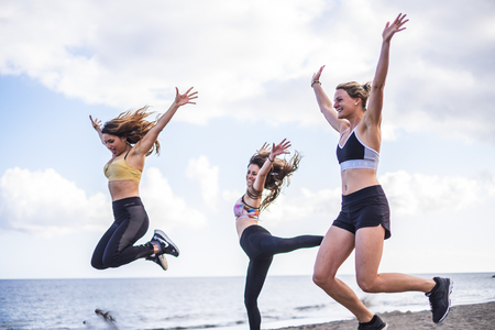 three beautiful bodie cacuasian girls jumping on the beach doing fintess workout. outdoor leisure sport activity for group of females people with ocean in backgroundの写真素材