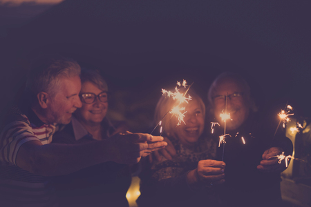 celebration time for party or new year eve for a group of senior friends with fire sparks. averybody together having  fun at night smiling and laughing. Group of four and party conceptの写真素材