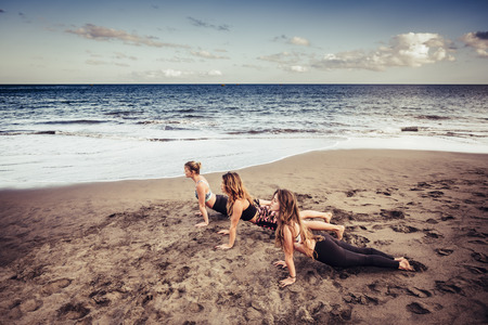 Three cacuasian young ladies doing pilates on the shore near the  waves and the ocean. outdoor leisure activity sport and lifestyle fitness for beautifl women. freedom and healthy. great landscape.の写真素材