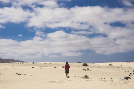 Lonely boy walking in the desert of fuerteventura. Barefoot on the soft yellow sand and dunes. Trekking and alternative travel and life concept.の写真素材