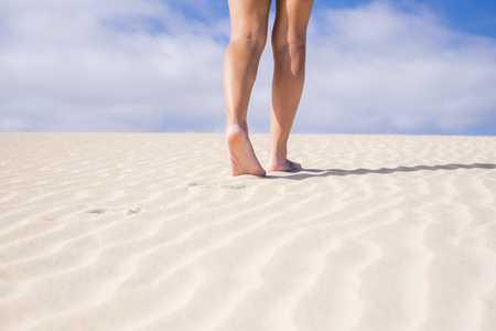 vacation nude, naturism concept with legs and feet walking in the soft sand with blue sky in the background. beautiful part of woman and freedom conceptの写真素材