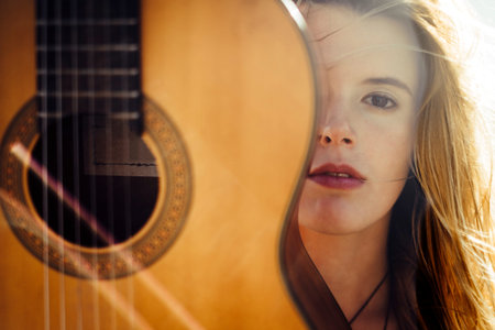close up portrait of beautiful blonde young woman with a guitar. yellow tones summer style. look at camera and backlightの写真素材
