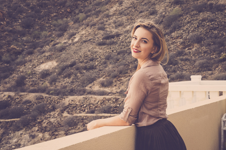 blonde girl with long hair, eyes closed, with blouse and pleated skirt in the terrace breathes caressed by the wind. Looking at the camera with sweetness. Warm filter and atmosphere.の写真素材