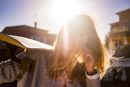 amazing beautiful nice blonde girl in backlight sunny portrait with her skateboard and wind in the hair. life and freedom independence concept.の写真素材