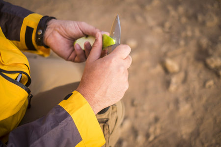 close up of human hands cutting a green apple with a knife outdoor during an adventure trekking...