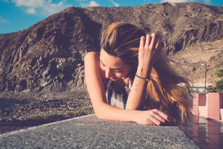 long hair spanish young woman erlaxing lay down on a wall near the beach. Sunlight on her beauty...