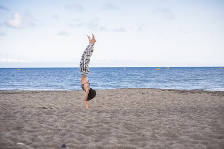 nice pretty caucasian girl standing up on the hand at the beach in outdoor summer leisure activity. ocean in the backgorund. enjoying life and balanced body in exercise. blue sky and waterの写真素材